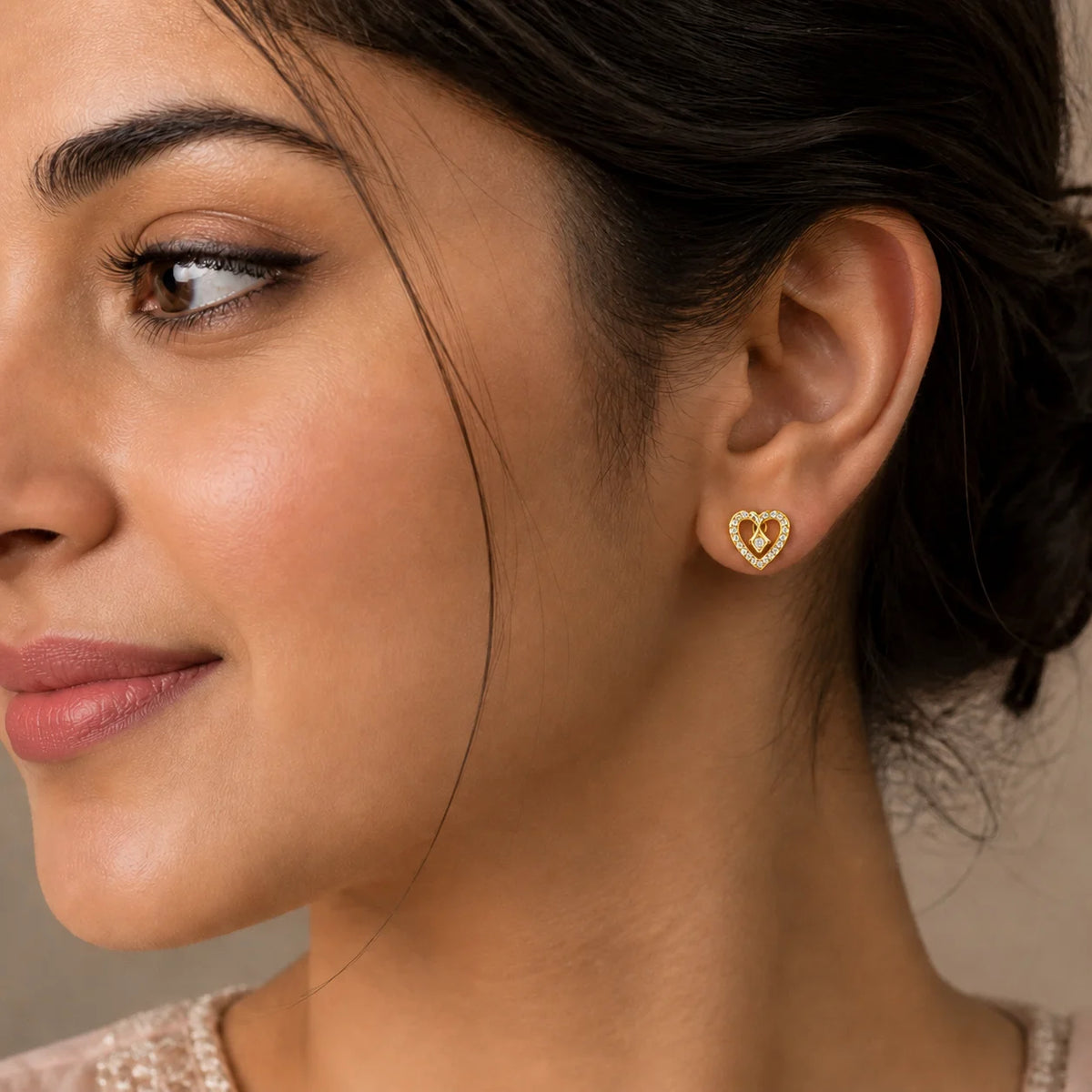 A close-up of a woman's ear wearing a small gold heart-shaped stud earring with a textured, dotted border.